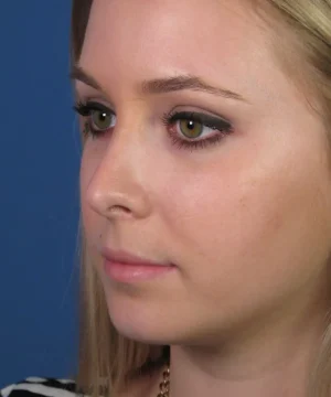 Side profile of a woman with long blonde hair and green eyes looking forward against a blue background.