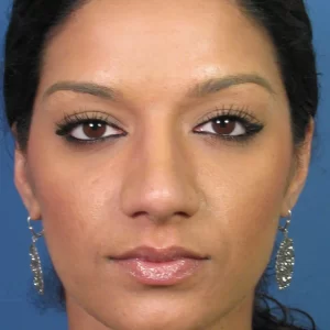 A person with earrings and neatly styled hair is facing forward against a blue background.