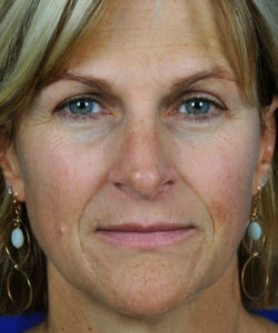 Close-up of a person with blonde hair, wearing oval earrings, looking directly into the camera.