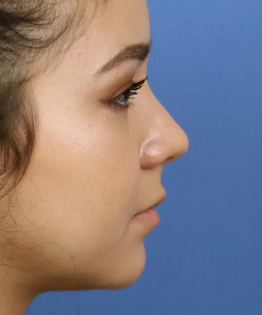 Profile view of a person with long lashes and neatly applied makeup against a blue background.