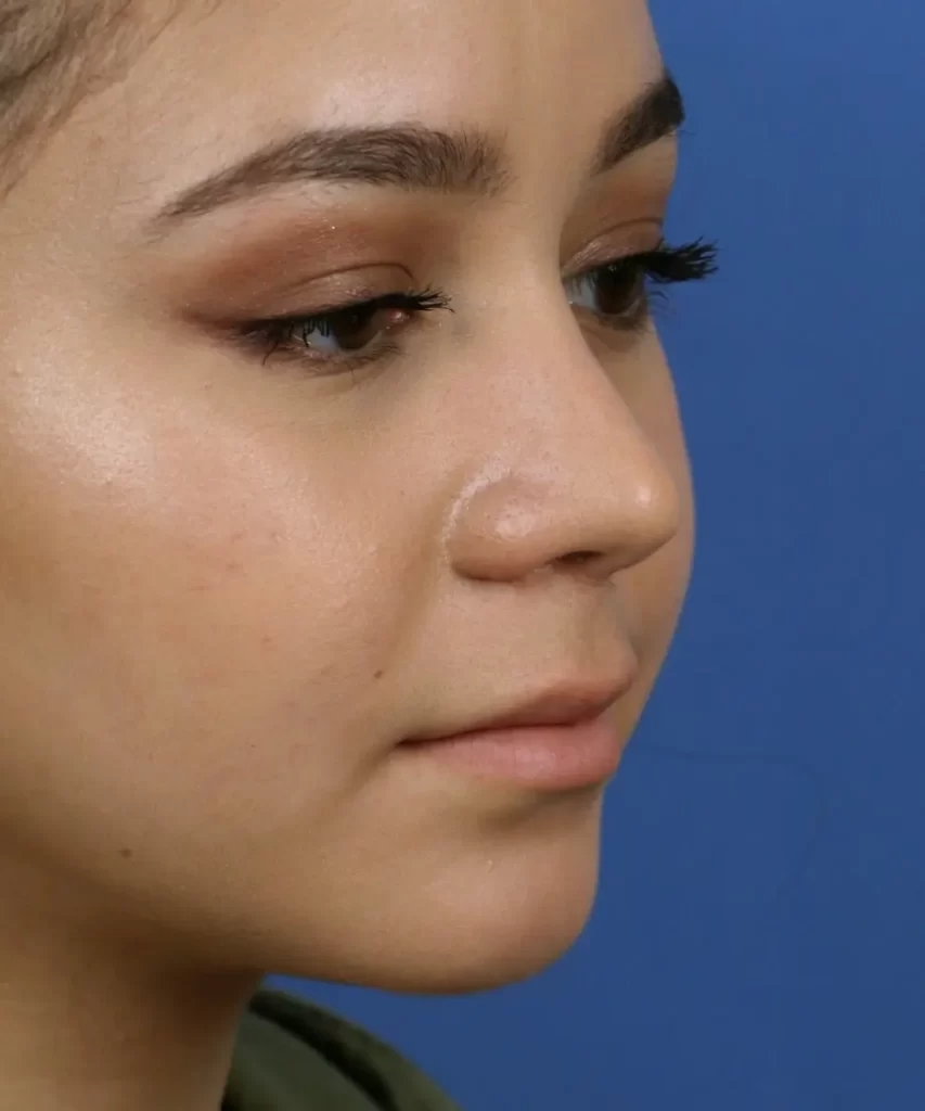 Close-up of a person with makeup, against a blue background, showing a side profile of the face with a calm expression.