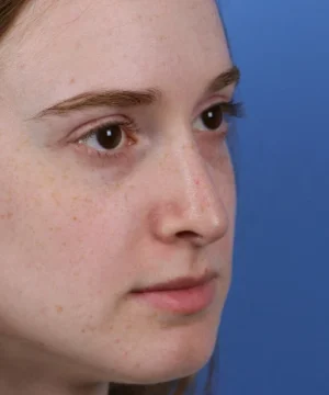 Close-up of a person with long brown hair against a blue background, looking forward. Their expression is neutral.