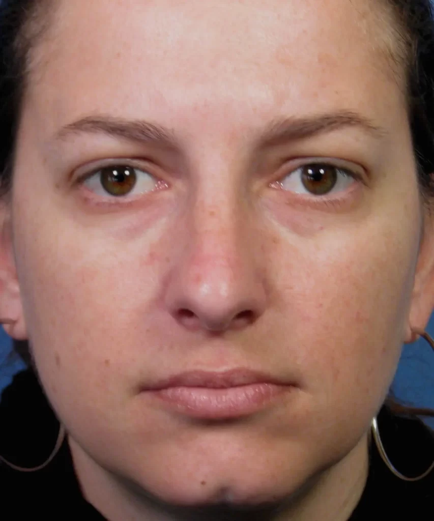 Close-up of a person with hoop earrings and a neutral expression against a blue background.