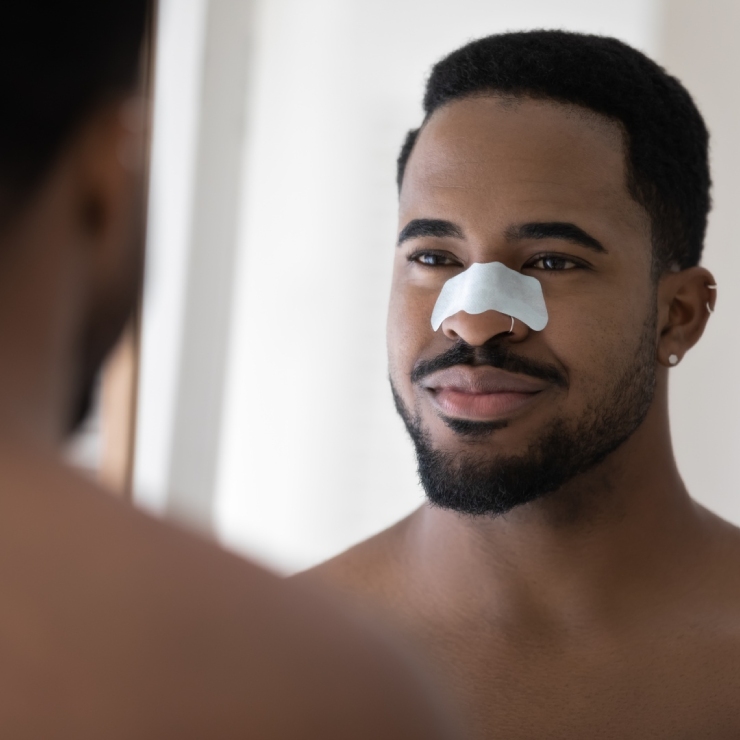 Man wearing a nose strip looks at his reflection in a mirror.