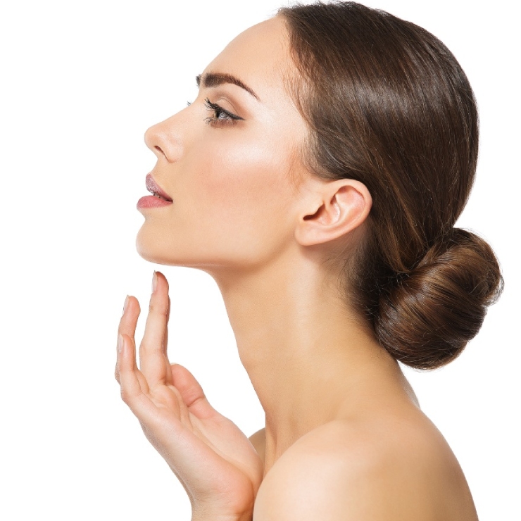 Profile view of a woman with her hair in a bun, touching her chin, on a white background.