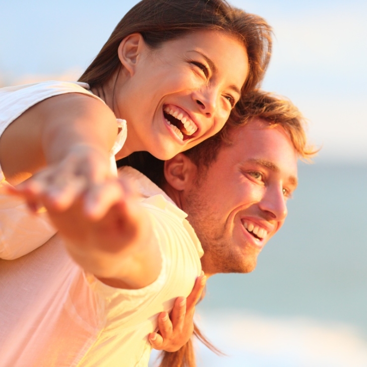 A smiling couple enjoying a playful piggyback ride on a sunny day at the beach.