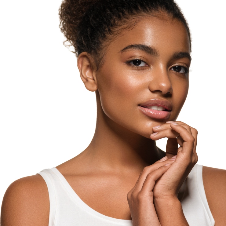 A person with curly hair poses against a white background, wearing a white top, with hands gently touching the face.