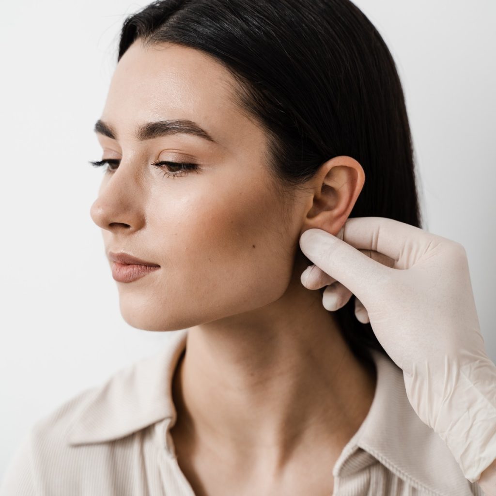 A woman's ear is examined by a gloved hand.