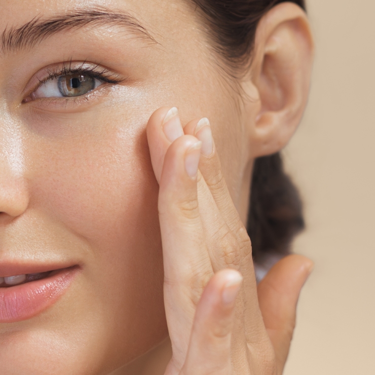 Close-up of a person applying skincare product to their cheek with fingers; shows part of the face and hand.