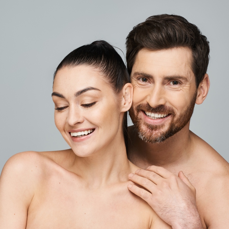 A smiling man and woman stand together against a gray background.