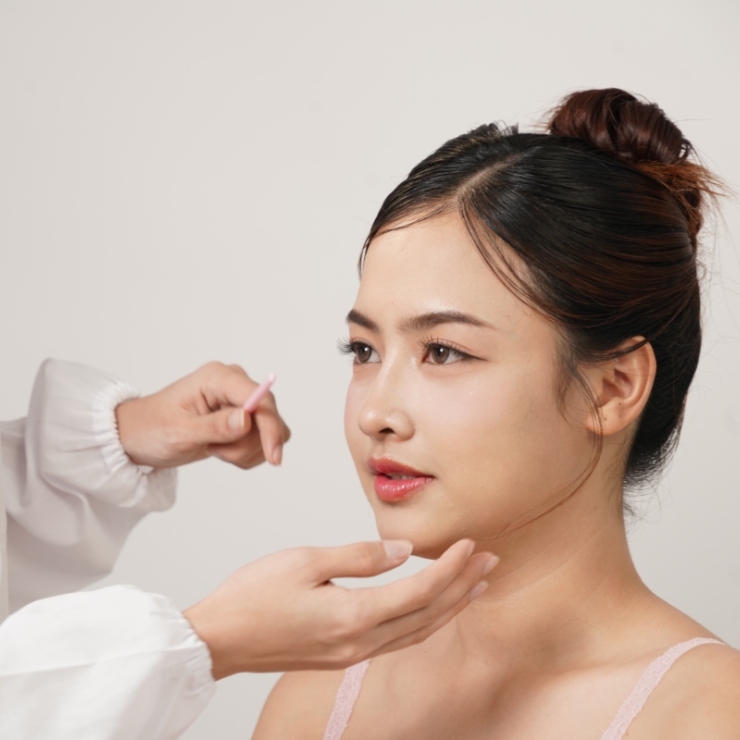 Person applying makeup to a woman's face using a brush, with the woman looking to the side.