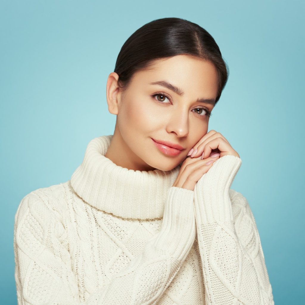 A person in a white turtleneck sweater poses against a blue background.