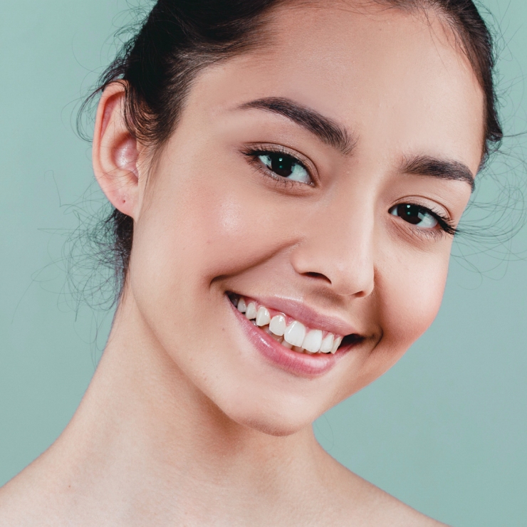 Smiling person with dark hair and clear skin against a light green background.