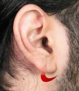 A close-up of a person's ear with long dark hair. A red swirl logo is positioned on the earlobe.