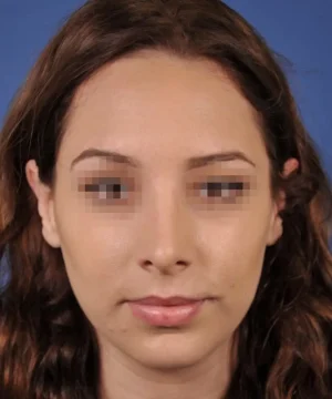 A person with long, wavy brown hair is facing the camera against a blue background. Their eyes are pixelated for privacy.