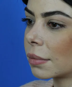 Close-up of a woman with dark hair and makeup, looking to the side against a blue background.