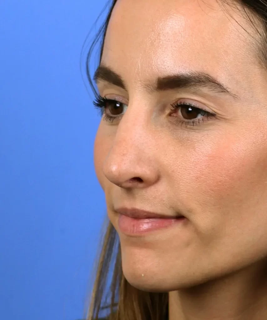 A person with long brown hair and neutral expression against a blue background, shown in profile.