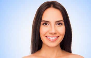 A woman with long dark hair smiles against a light blue background.