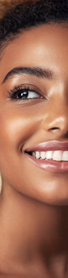 Close-up of a person smiling, showing smooth skin and teeth. The image focuses on the right side of their face, highlighting their eye, cheek, and part of their lips.